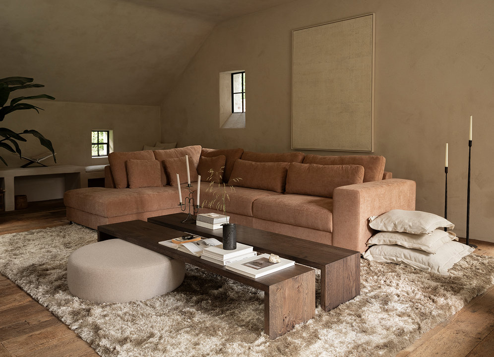 Woonkamer met roze hoekbank, twee rechthoekige salontafels, vloerkleed en poef